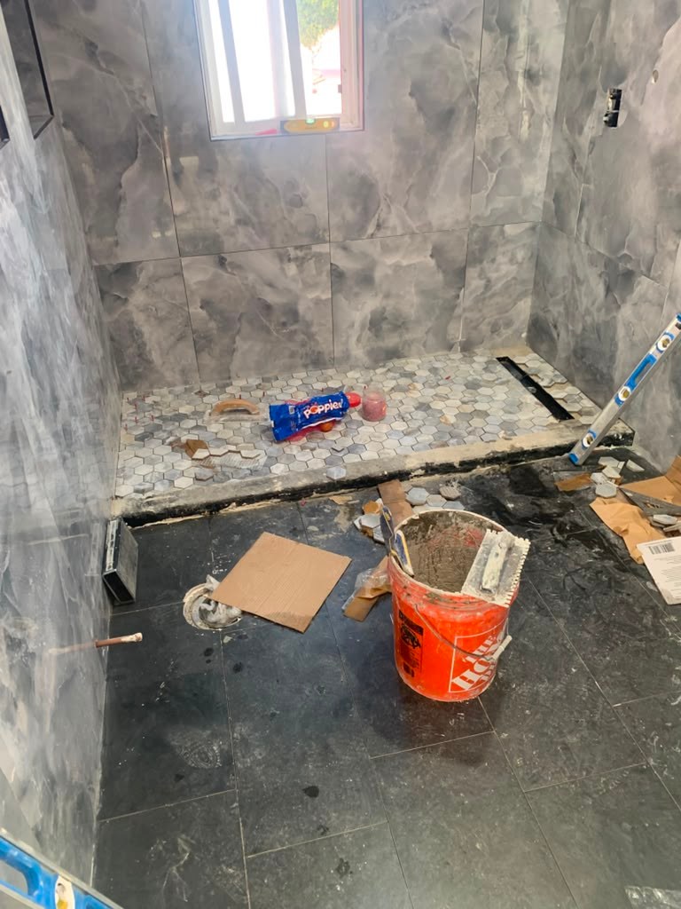 A partially renovated bathroom with gray marble walls, a mosaic tile floor, construction debris, and a bucket of paint.