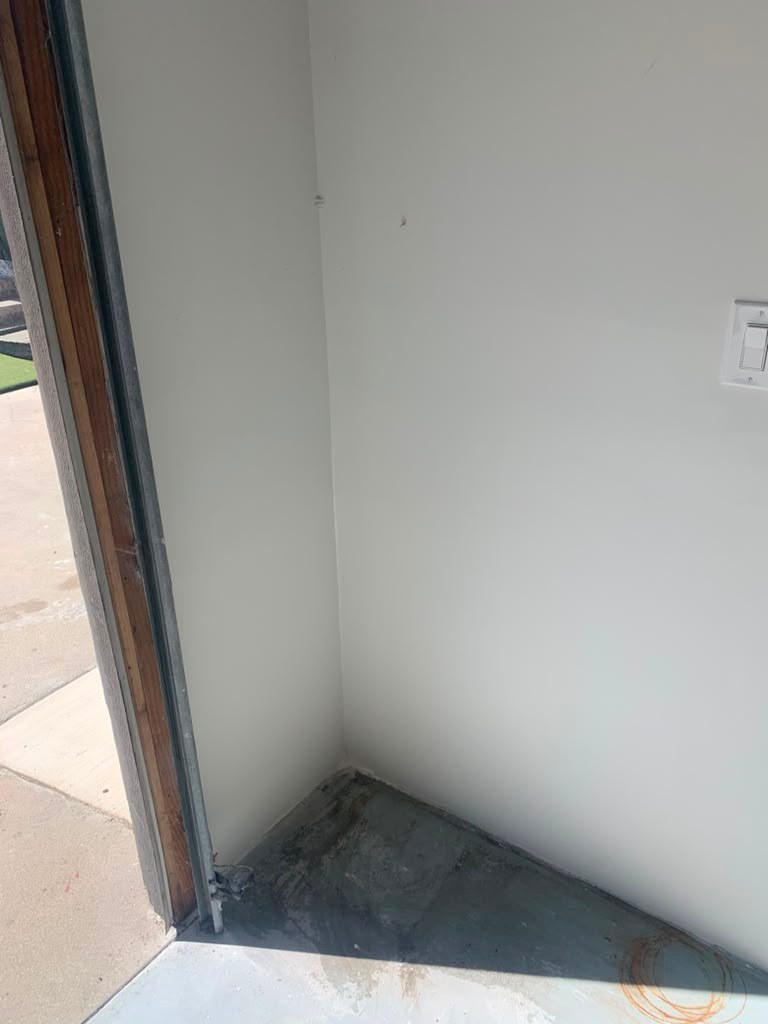 A corner of a garage showing a wall with visible water damage, peeling paint, and a concrete floor.