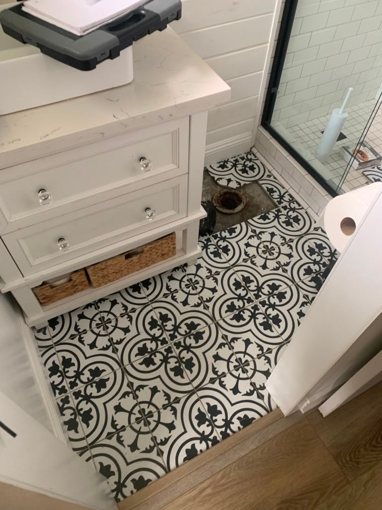 Bathroom floor featuring black and white patterned tiles, a white cabinet with drawers, and a visible drain in the corner.