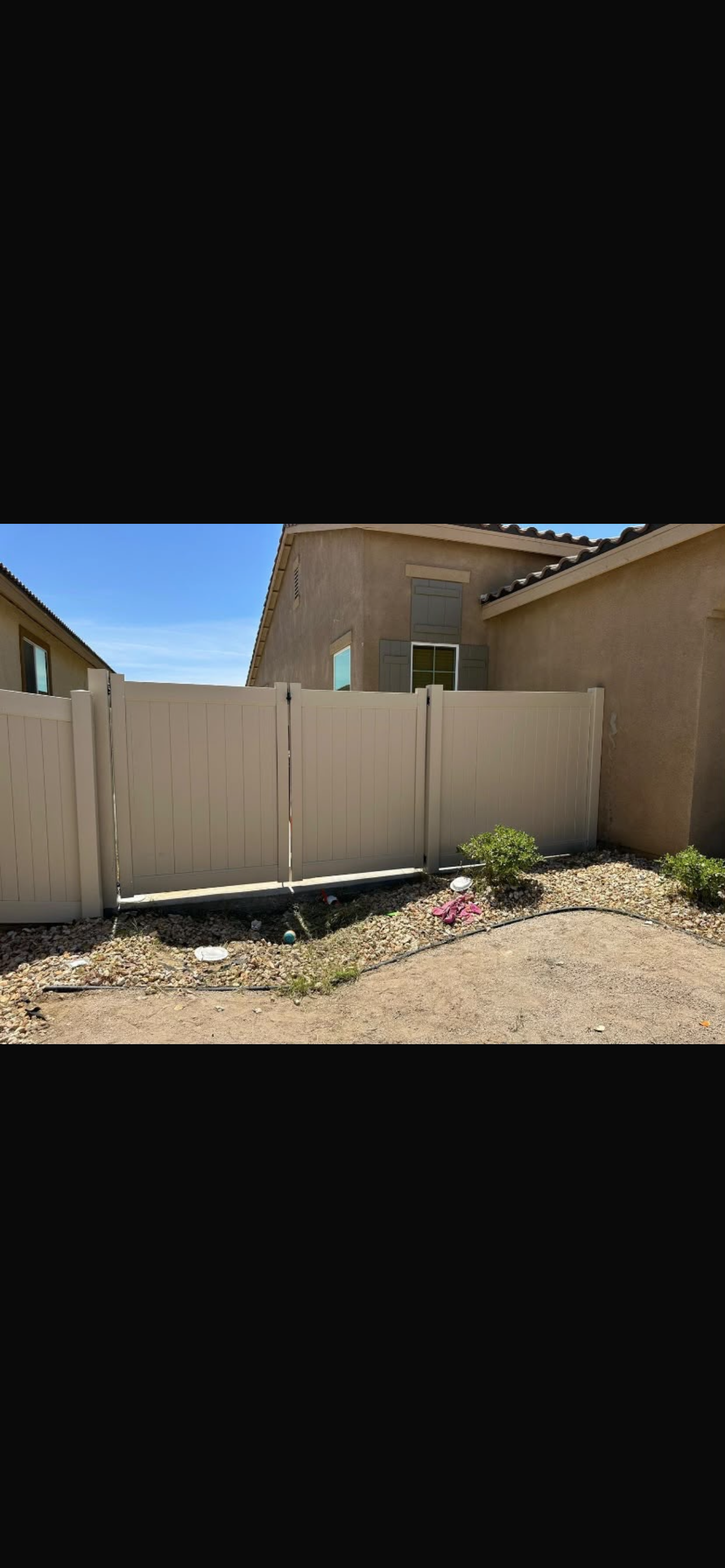 Vinyl fencing in a residential setting, with a double gate visible, surrounded by gravel and a house in the background.
