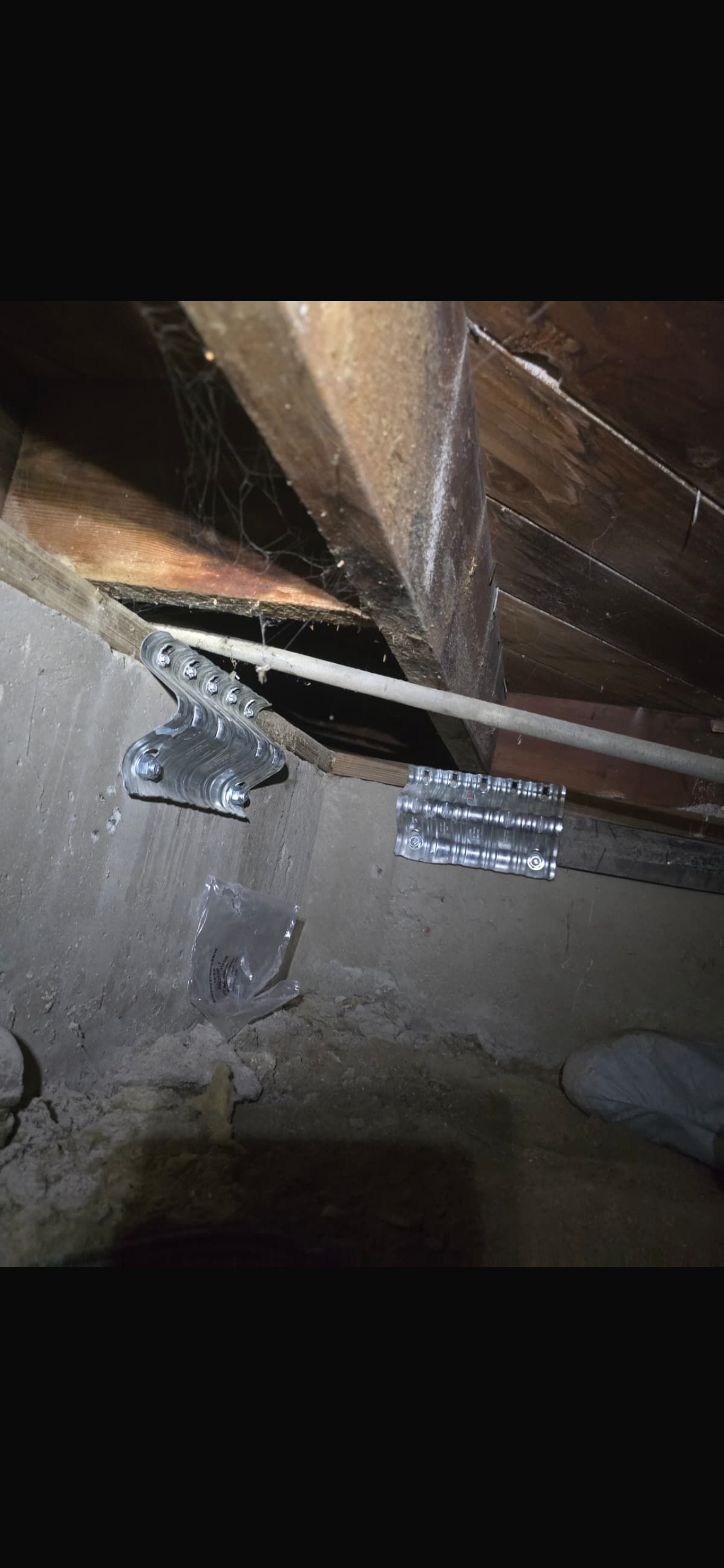 Close-up of a wooden foundation with metal brackets and a clear plastic sheet, showing structural support and maintenance details.
