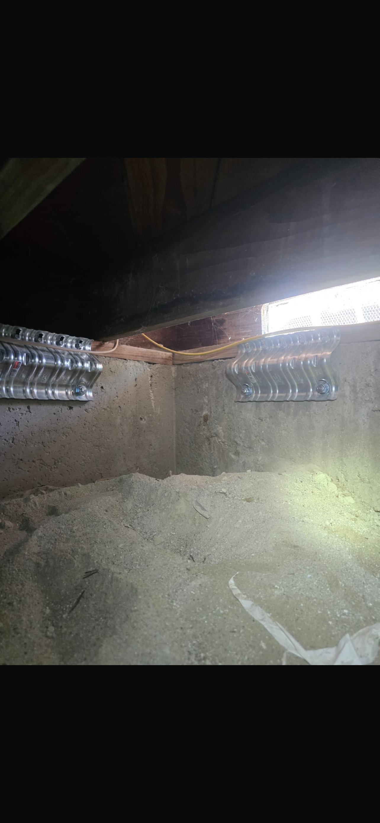 View of a foundation space showing exposed beams, gravel, and ductwork, highlighting maintenance and retrofitting conditions.
