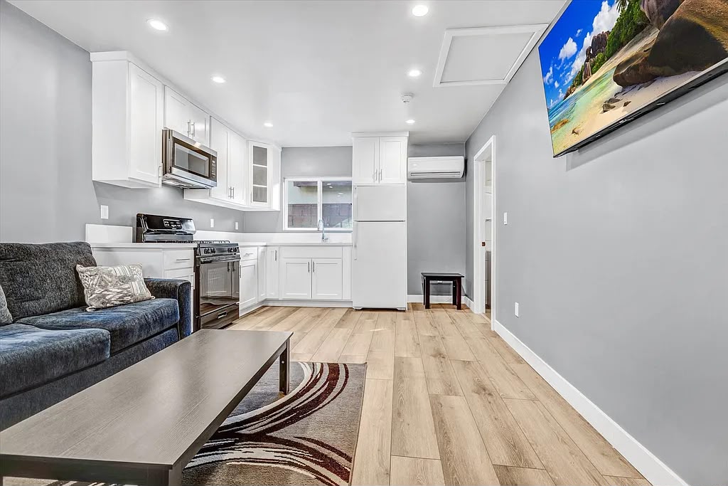 Remodeled open kitchen and living area with white cabinets, wood-look floors, and a mounted TV