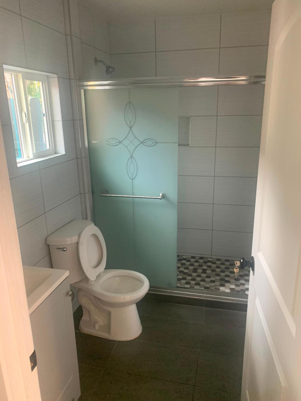 Remodeled bathroom with teal glass accent tile, a toilet, and a natural-light window