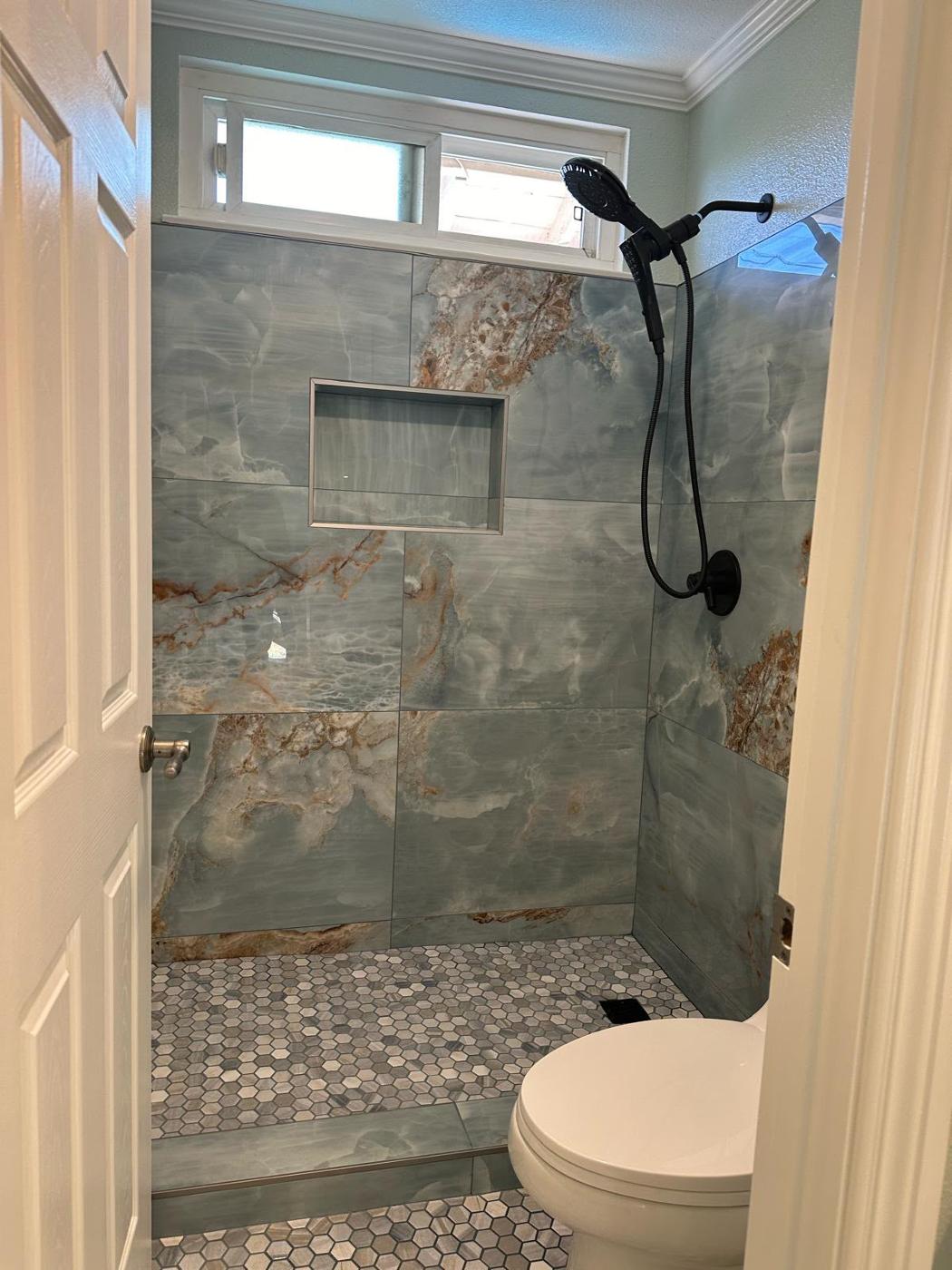 Remodeled bathroom with a natural stone-look tiled shower and a bright window