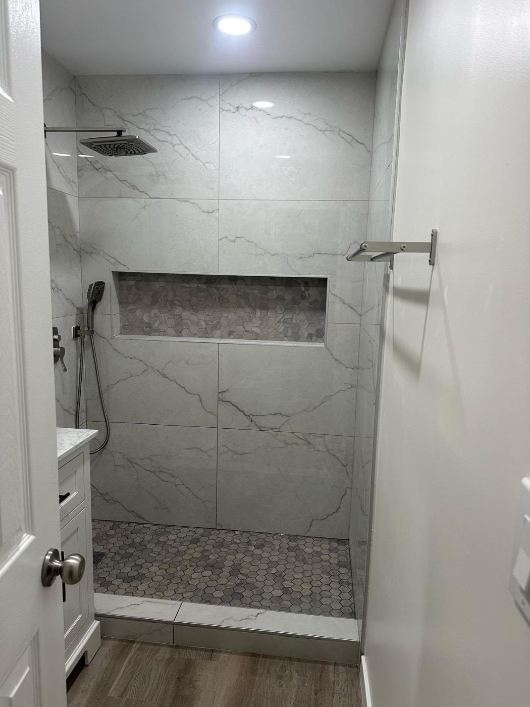 Completed walk-in shower with large grey tile, frameless glass, and a built-in niche