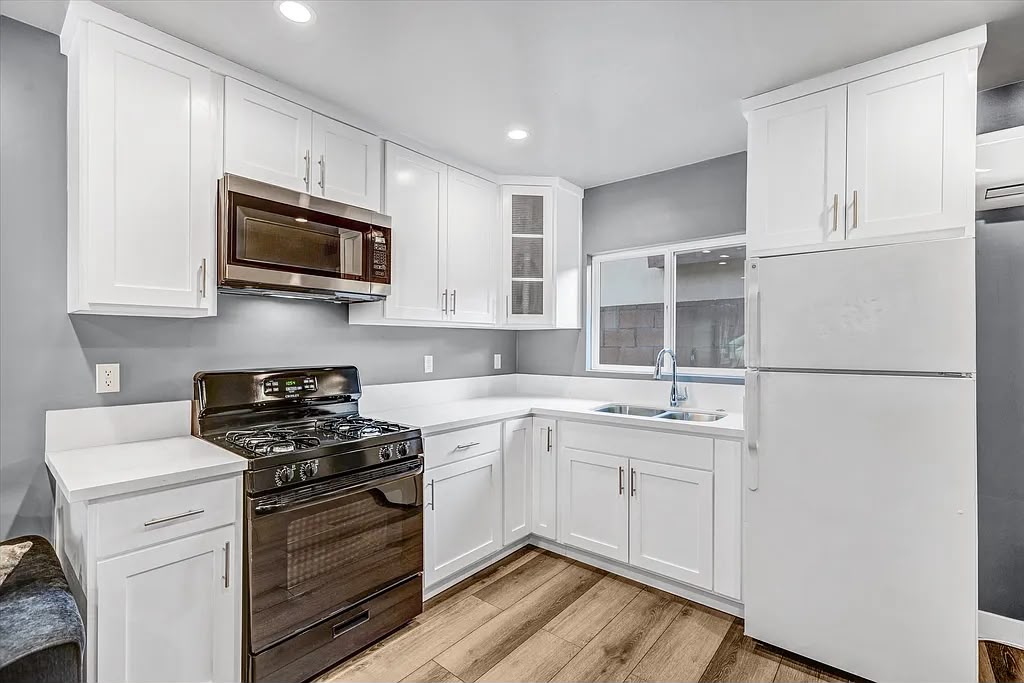 Finished white kitchen with shaker cabinets, a black range, and light wood-look flooring
