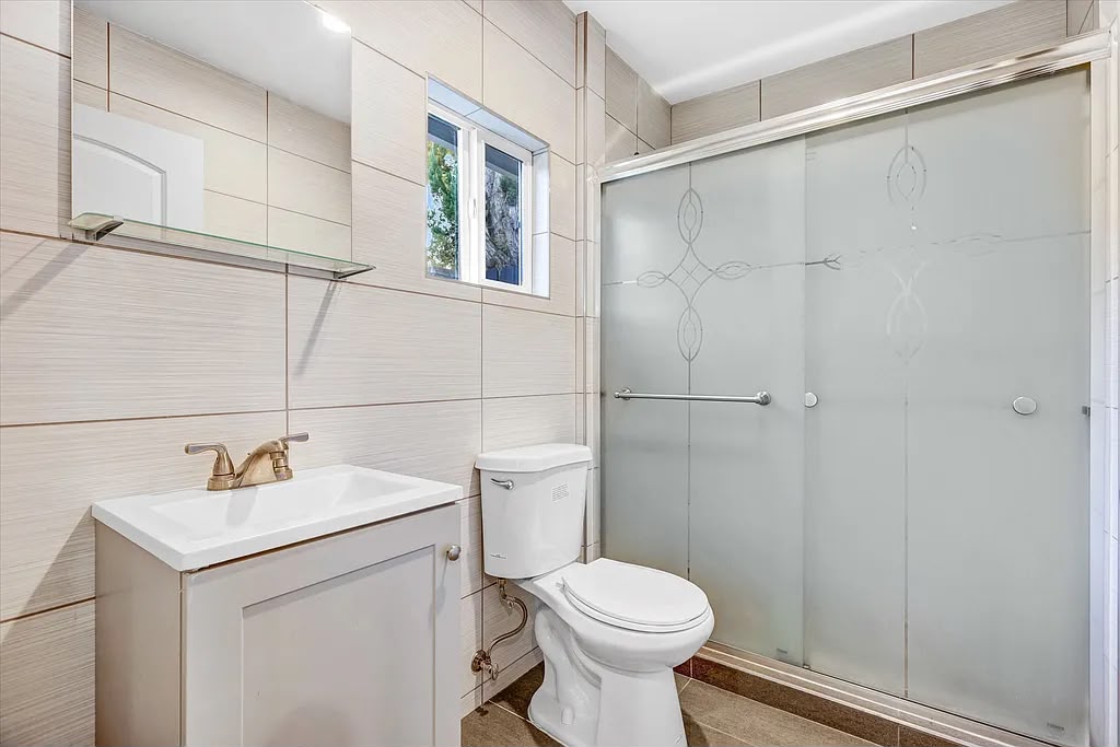 Remodeled bathroom with a white vanity, toilet, and a glass-enclosed shower